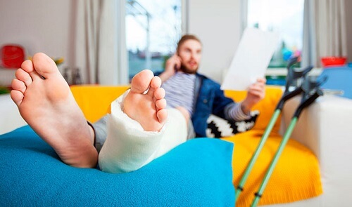 man with leg in cast sitting by crutches looking at medical bills